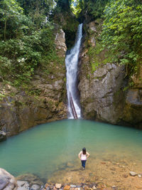 Full length of woman standing on rocks by waterfall