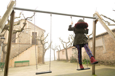 Young girl sheltered in an abandoned swing set with hood, unrecognisable.