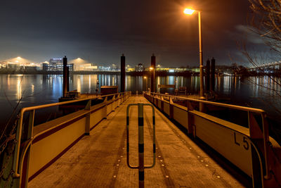 Illuminated pier over river against sky at night