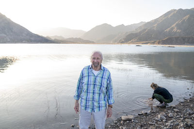 Man smiling while standing outdoors in nature near a lake.