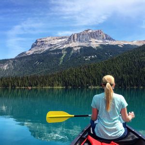 Rear view of woman sitting on canoe in lake against mountain