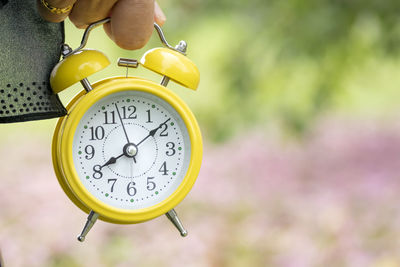 Cropped hands holding yellow alarm clock outdoors