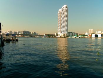 Buildings by river against clear sky in city