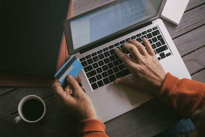 Senior man's hands doing online payment with credit card through laptop at home