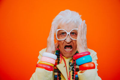 Portrait of angry senior woman wearing eyeglasses against red background