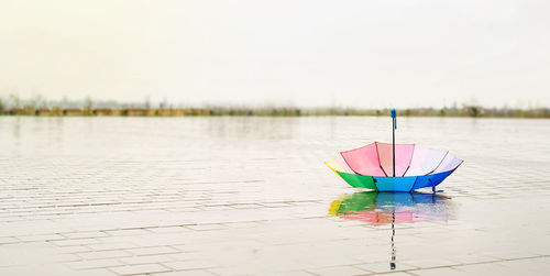 Rainbow colored umbrella lying in puddles on the wet street ground. copy space