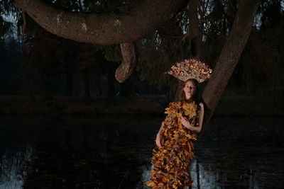 Young woman with autumn leaves against tree trunk by lake