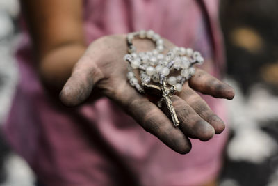 Close-up of dirty hand holding rosary beads outdoors