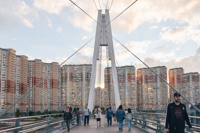 People walking on bridge in city against sky