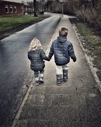 Rear view of mother and daughter walking on road