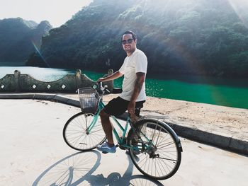 Portrait of man with bicycle standing on road by sea