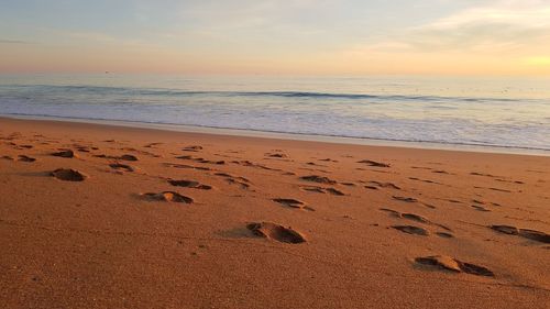 Footprints on sand at beach against sky during sunset