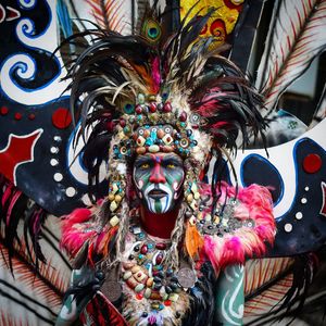 Portrait of man wearing multi colored feathers with face paint