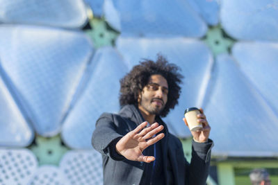 Portrait of man gesturing stop sign while having coffee in city