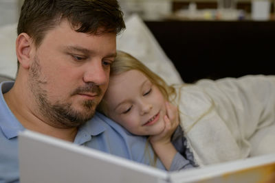 Dad entertains the child during illness, he looks, reads a book, a photo book with his daughter home