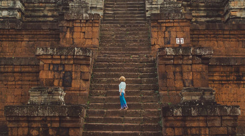 Full length rear view of woman against brick wall of building