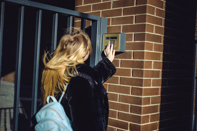 Close-up of woman using phone while standing on brick wall