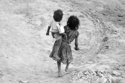 Girl carrying her brother while walking on field