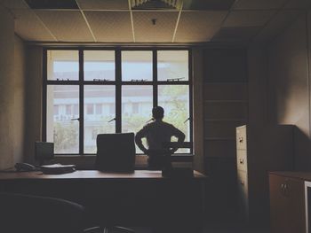 Rear view of businessman standing against window in office