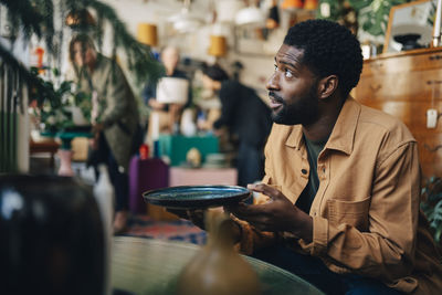 Man looking away while holding plate at antique store