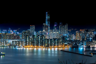 Illuminated buildings by river against sky at night