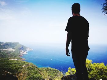 Rear view of man standing on mountain against sea