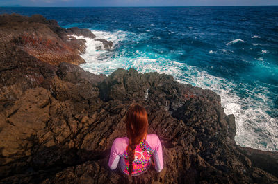 Rear view of woman sitting on rock at beach