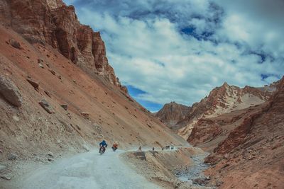 People walking on rock formation against sky