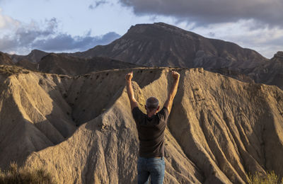 Rear view of man with arms raised against mountains, in tabernas desert, almeria, spain