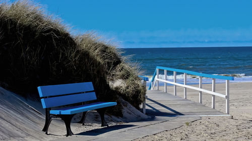Deck chairs on beach against clear blue sky