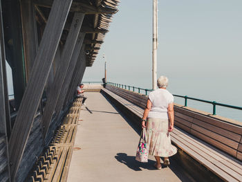 Rear view of woman on footbridge against sky