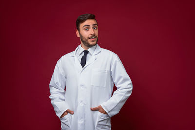 Portrait of young man standing against red background