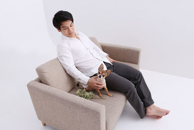 Full length of man sitting with dog on sofa against white background