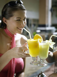 Happy woman toasting drink with cropped friend sitting on table at restaurant