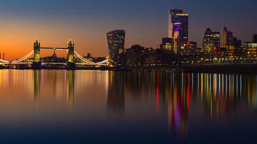 Illuminated buildings by river against sky at night