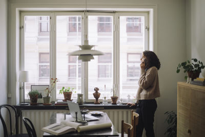 Side view of woman looking through window