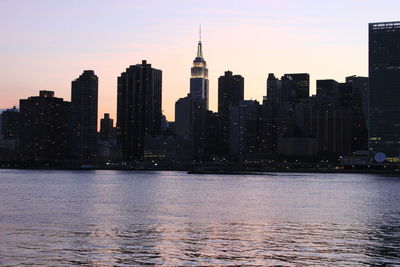 Modern buildings by river against sky during sunset