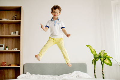 A little boy jumps on his bed in the bedroom and laughs.