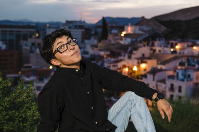 Young transgender man looking up while posing outdoors at sunset.