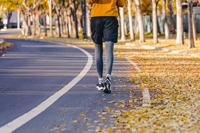 View from the back of unrecognizable man jogging outdoors in the fall. yellow leaves on the street,