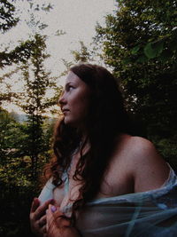 Woman looking away while standing against trees