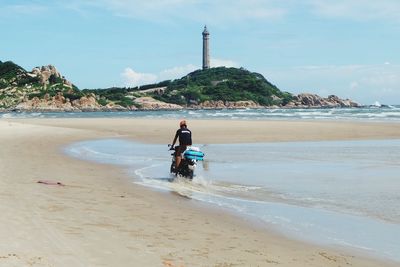 Rear view of man riding motorcycle at beach against sky