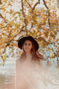 Portrait of young woman standing against tree