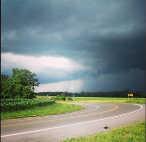 Road passing through field against cloudy sky