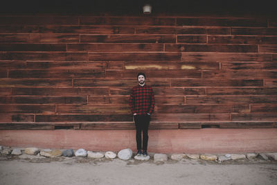 Portrait of man with hands in pockets standing on rock against wall