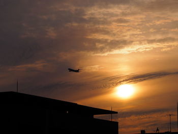 Low angle view of silhouette airplane flying against sky during sunset