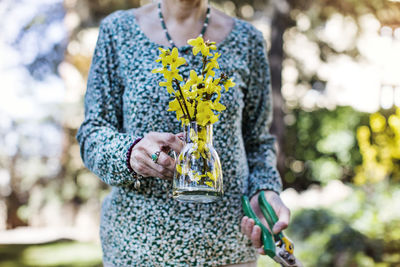 Midsection of senior woman holding flower vase and pliers at yard