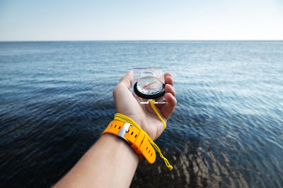 A man's hand with a wristwatch bracelet holds a magnetic compass against the background of the sea