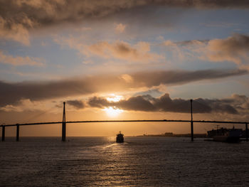 Silhouette bridge over sea against sky during sunset