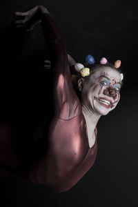 Portrait of woman with face paint wearing clown costume against black background
